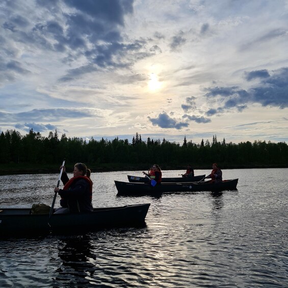 People canoeing on a calm lake with a forest in the background and the sun setting. 4