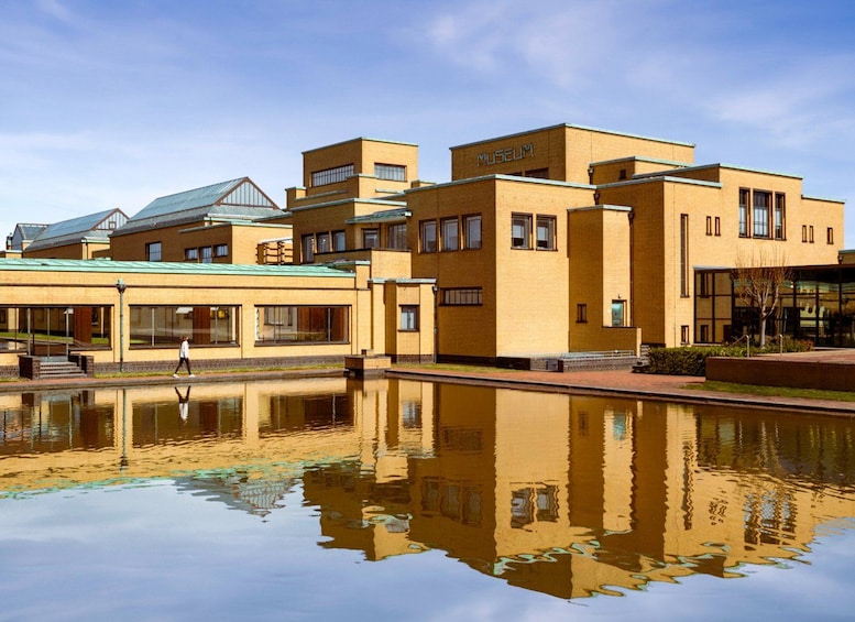 Ein Museum mit Spiegelung im Wasser, eine Person geht vorbei, und ein klarer Himmel. 1