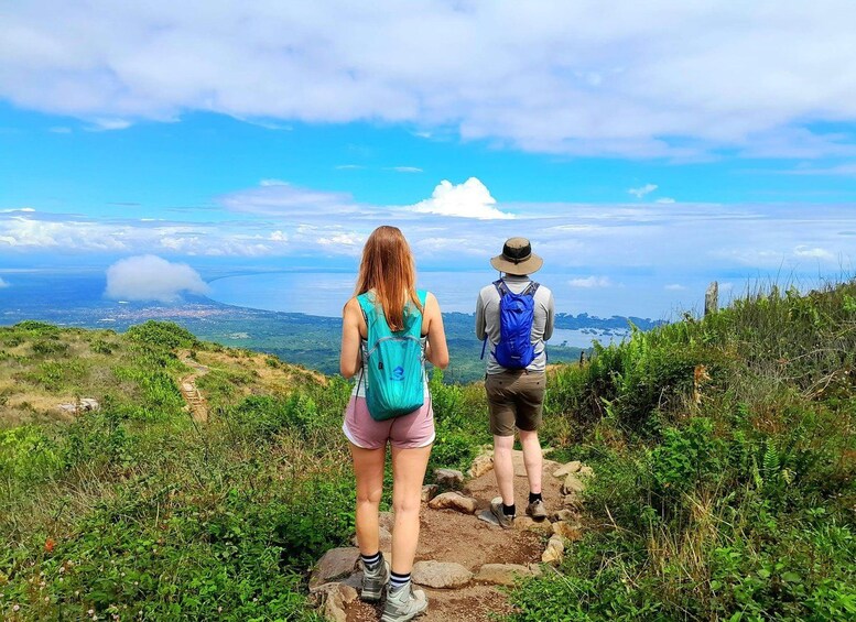 Two hikers on a rocky trail with a scenic view of a coastline and clouds in the sky. 3