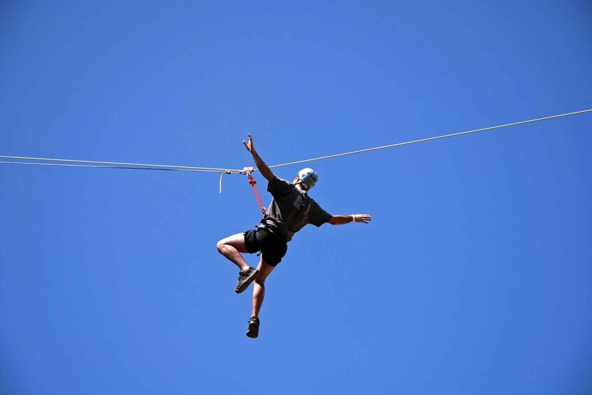 A person performing a trapeze act against a clear blue sky. 1
