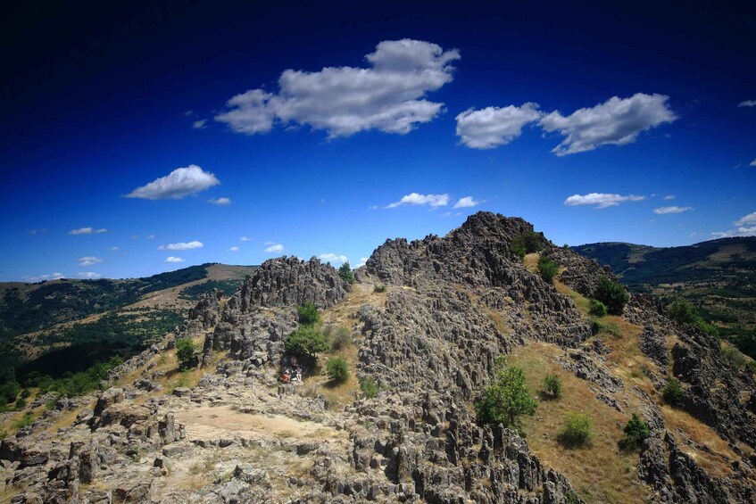 Un paysage montagneux accidenté, avec des affleurements rocheux et une végétation clairsemée, sous un ciel bleu dégagé. 4