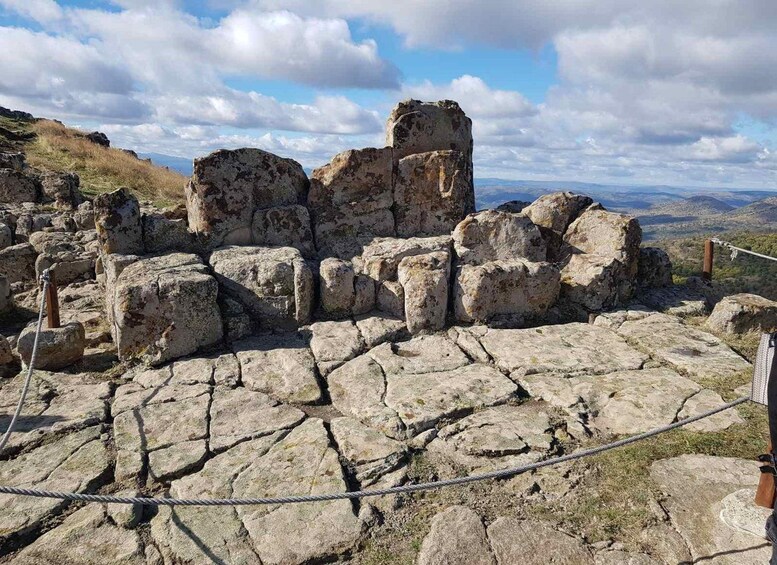 Vestiges de constructions anciennes en pierre, délimités par une barrière en corde, et entourés d’un paysage montagneux. 2