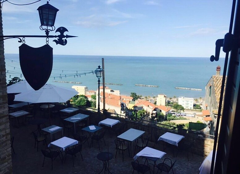 An outdoor dining area with tables and chairs, overlooking a coastal view with buildings and the sea. 3