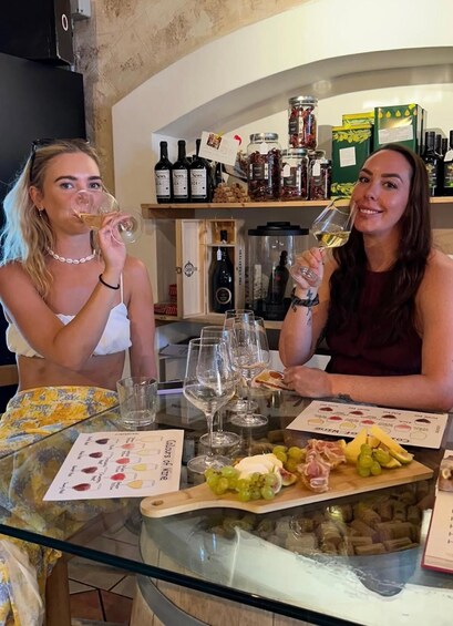 Two people sitting at a table with wine glasses, a menu, and a selection of grapes and cheese. 2