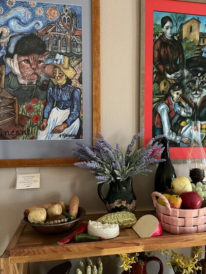 Une peinture représentant un chat, un vase de fleurs et un panier de fruits sur une table en bois. 3