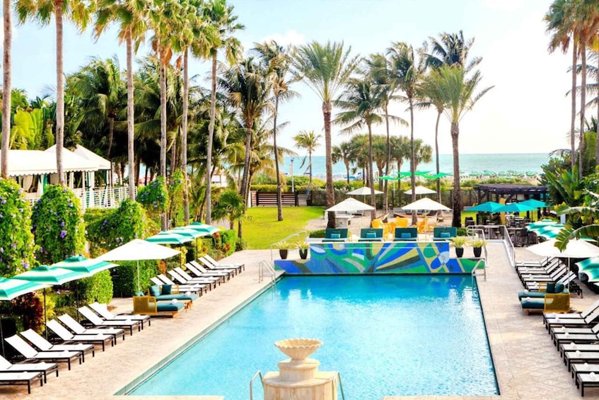 A pool area with lounge chairs and umbrellas, surrounded by palm trees and a view of the ocean. 3