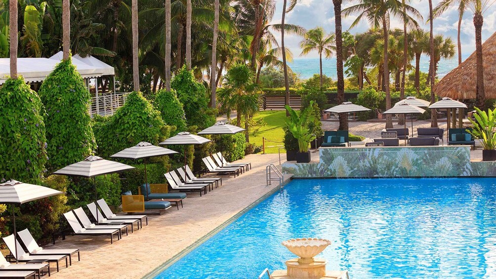 A poolside area with lounge chairs and umbrellas, surrounded by palm trees and a view of the ocean. 1