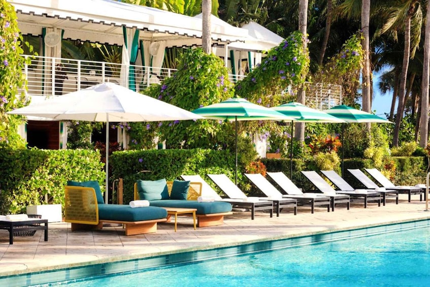A poolside area with lounge chairs and umbrellas, surrounded by lush greenery and palm trees. 2