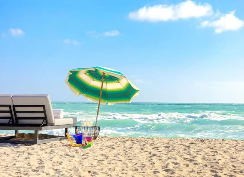 A beach with a green and white striped umbrella, a white lounge chair, and a bucket with a shovel. 4