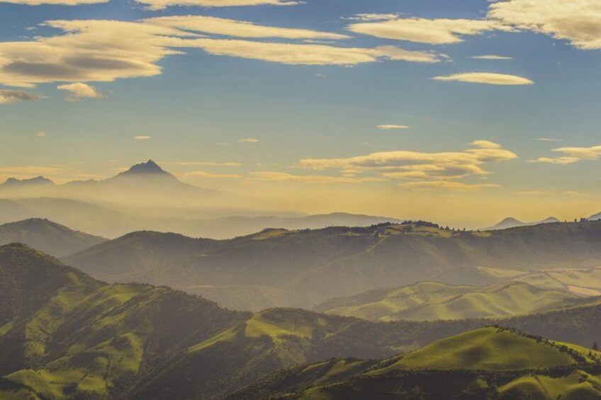 A mountainous landscape with rolling hills and a prominent peak in the distance. 2