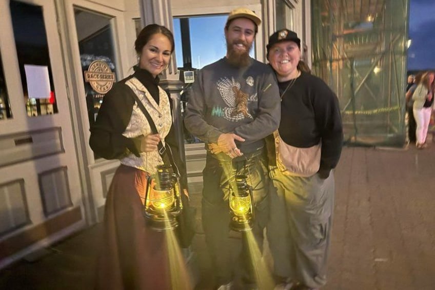 Three people holding lanterns in front of a building with a sign. 3