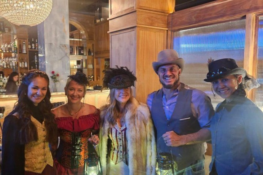 A group of people in a bar setting with wooden decor and a chandelier. 1