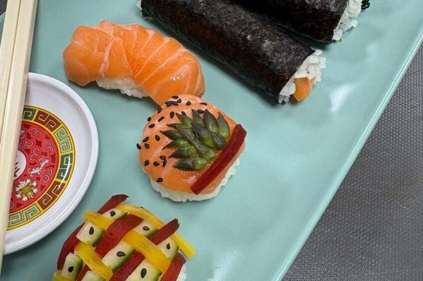 Sushi on a plate with chopsticks, a small bowl, and a decorative item. 2