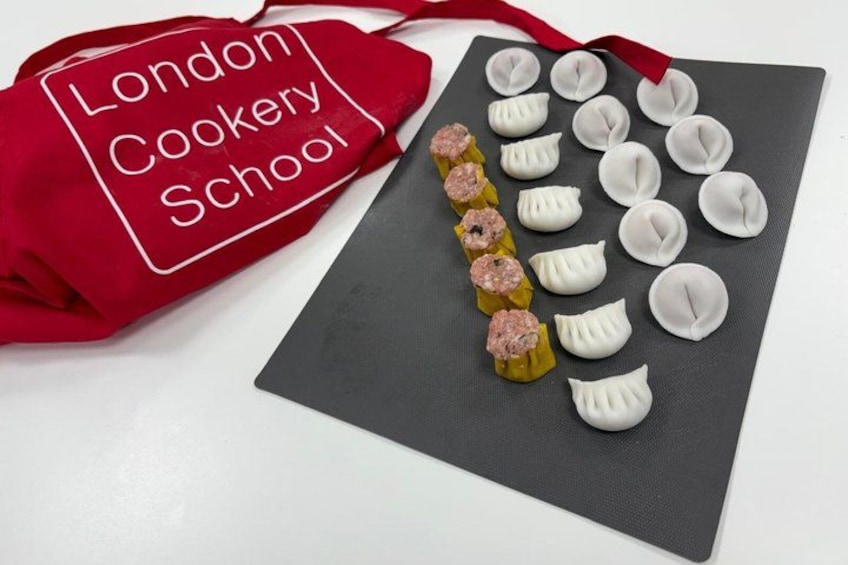 A red apron with 'London Cookery School' text, a black cutting board with dumplings, and a row of dumplings with pink filling. 1
