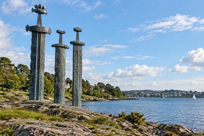 Three swords on a rocky shore with a sailboat in the background. 5