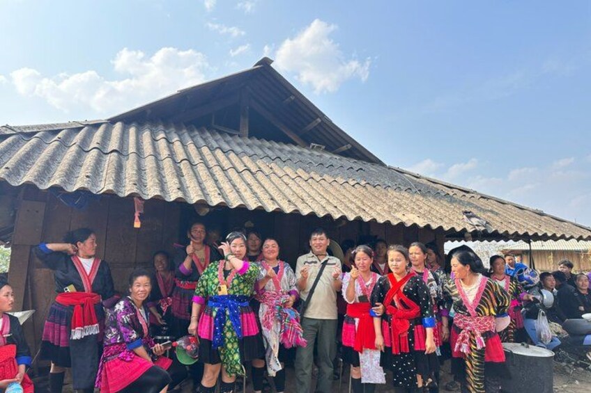 A group of people in traditional attire standing in front of a rustic building with a corrugated metal roof. 4