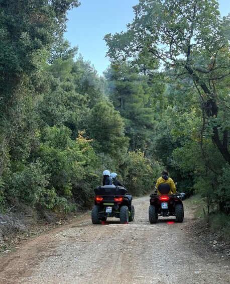 Two people riding ATVs on a gravel path surrounded by dense greenery. 1