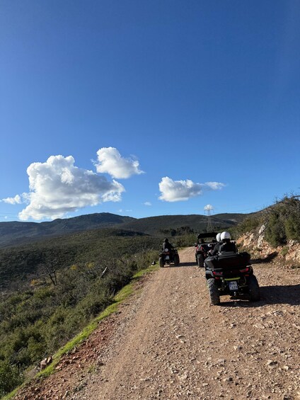 Two ATVs on a gravel road with a mountainous landscape in the background. 3