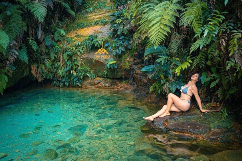 A person sitting on a rock by a clear water body surrounded by dense green foliage. 2