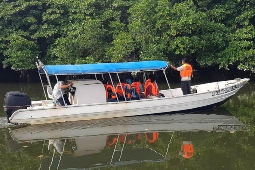 A boat with a blue canopy, people wearing orange life jackets, and a person steering. 1