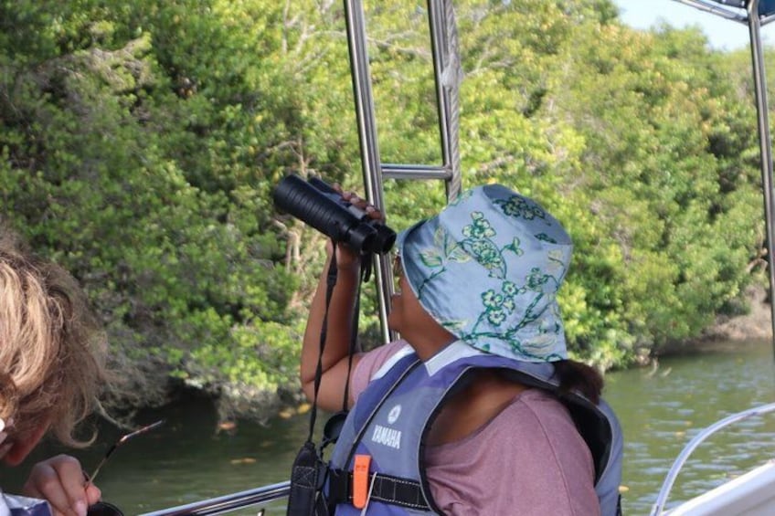 A person on a boat, wearing a life jacket and binoculars, looking at the water. 5