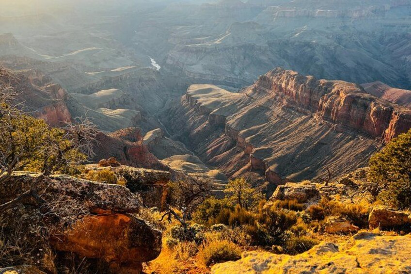 A canyon landscape with layered rock formations, sparse vegetation, and a river running through the valley. 2
