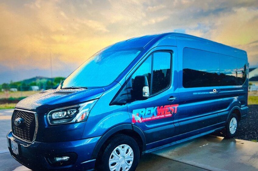 A blue van parked on a concrete surface with a cloudy sky in the background. 1