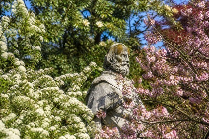 A statue surrounded by blooming trees and flowers. 1
