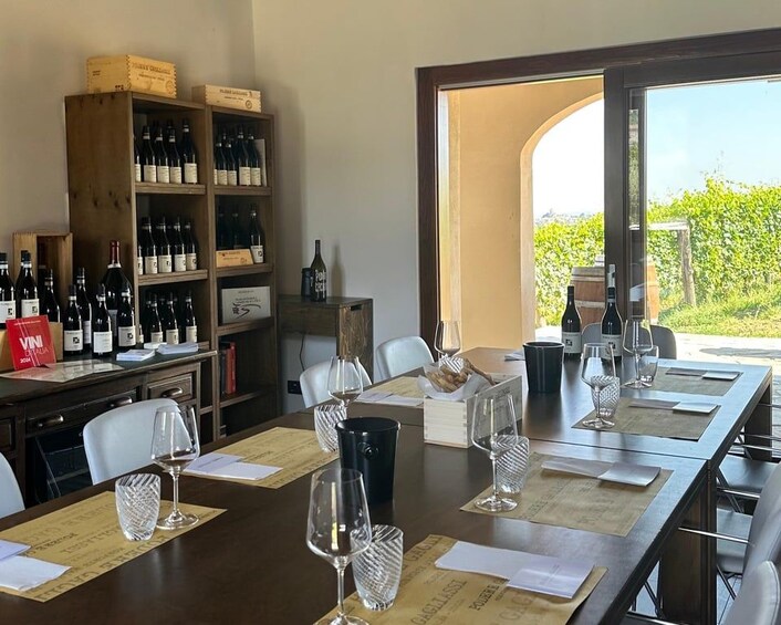 Una mesa de comedor lista para una comida, con copas y botellas de vino, un botellero de madera y vistas al exterior con vegetación. 4