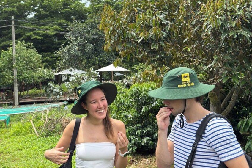 Two people wearing hats, one in a white dress and the other in a striped shirt, standing in a lush garden with trees and a pool in the background. 5