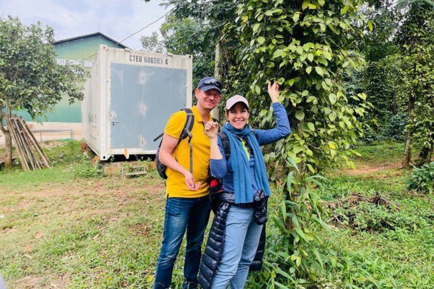 Two people standing outdoors with a green building and a tree in the background. 3