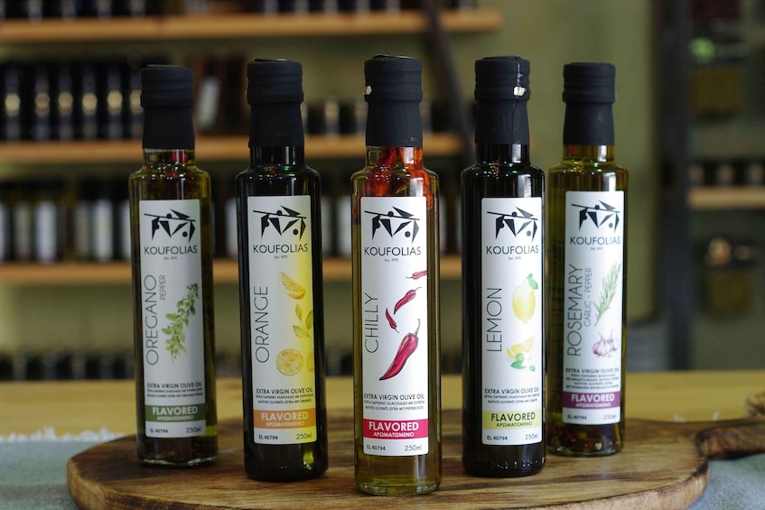 Five bottles of KOUFOLIAS olive oil with different flavors on a wooden surface. 5