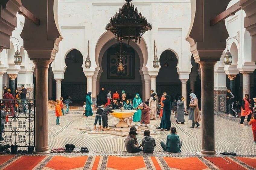 A courtyard with arches, a fountain, and people sitting and walking. 3