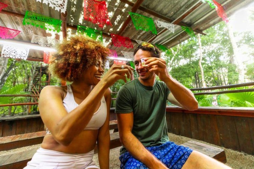 Two people sitting on a wooden bench under a shelter with colorful paper decorations. 3
