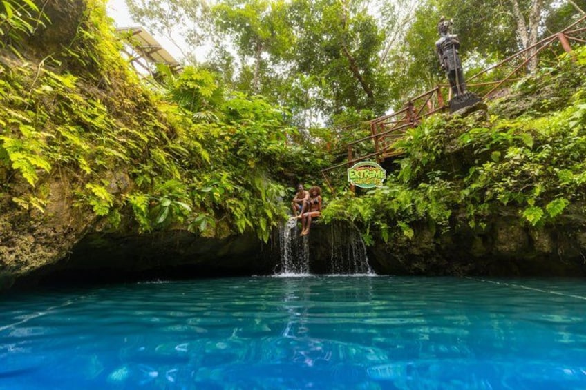 A natural pool with a waterfall, surrounded by lush greenery and a statue. 5
