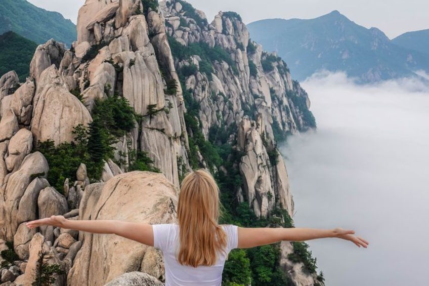 A person with arms outstretched facing a rocky mountain landscape. 1