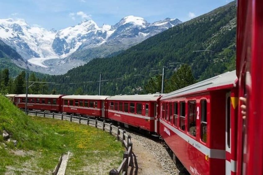A red train on tracks with snow-capped mountains in the background. 3