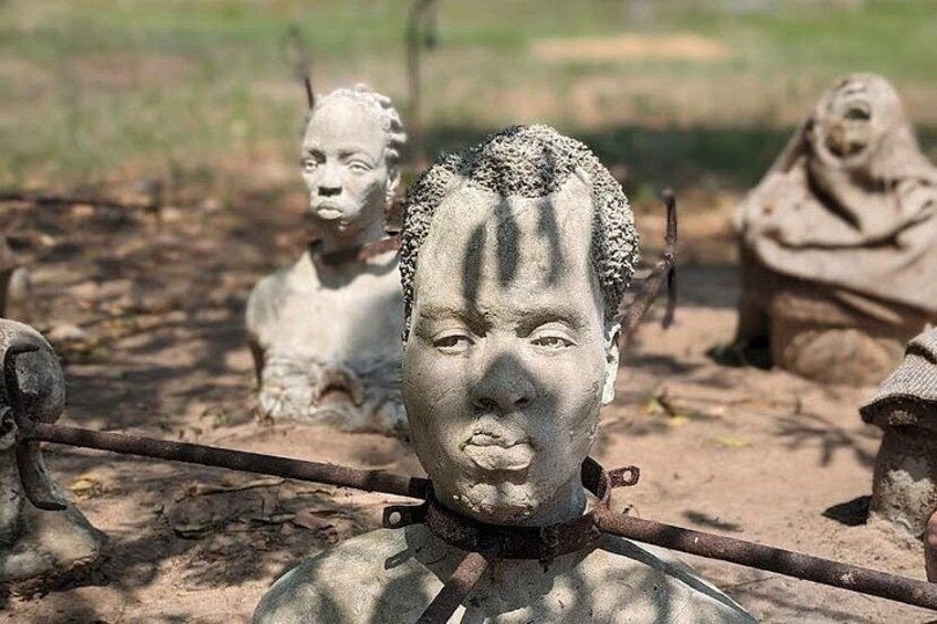 A sculpture of a person with a chain around the neck, surrounded by other similar sculptures in an outdoor setting. 3
