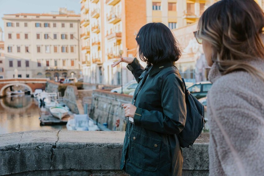 A person standing on a bridge overlooking a canal with boats, with buildings in the background. 4