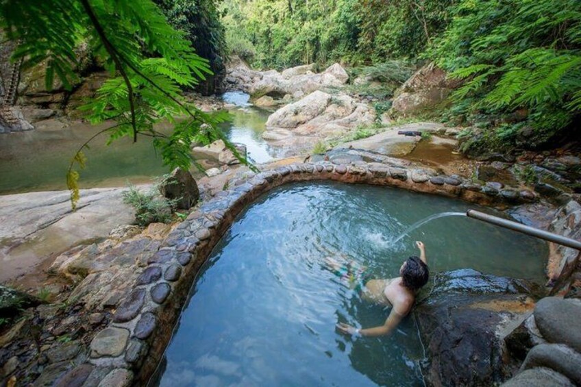 A person in a natural hot spring surrounded by rocks and greenery. 5