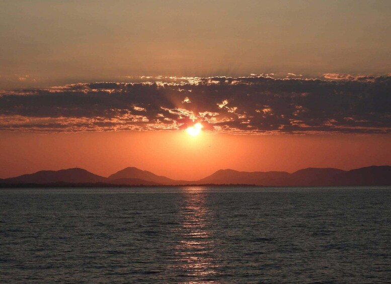 A sunset over a body of water with mountains in the background. 1
