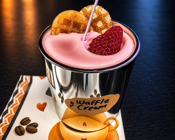 A metallic cup with a waffle cream drink, waffle pieces, and a raspberry on a napkin with coffee beans. 4