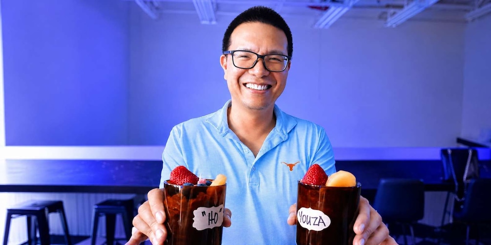 A person holding two drinks with 'HO' and 'Youza' labels, in an office environment with blue lighting. 1