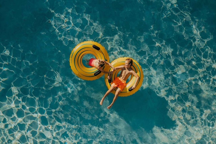 Two people floating on yellow inflatable rings in a clear blue pool. 1