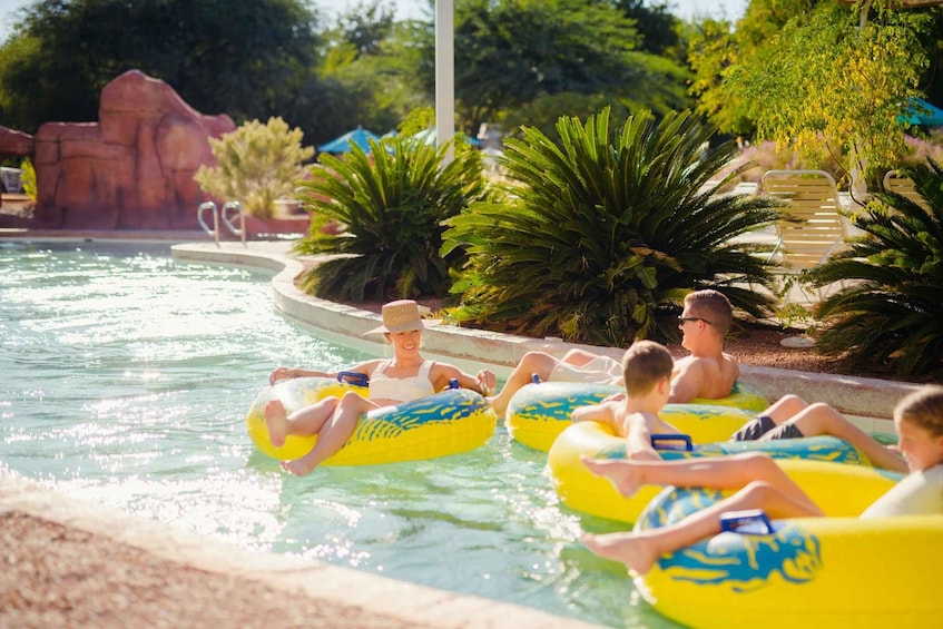 People floating on water tubes in a pool with palm trees and a rock formation in the background. 4