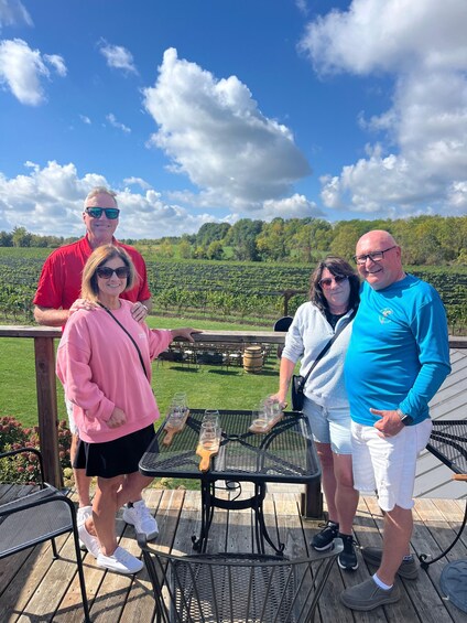 Four people standing on a wooden deck with a vineyard in the background. 5