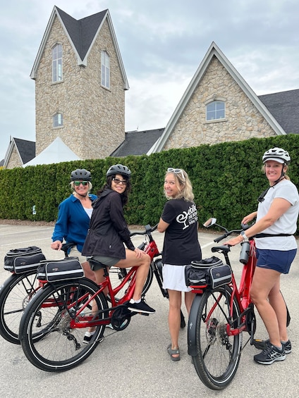 Four people on bicycles in front of a stone building with a steep roof. 2
