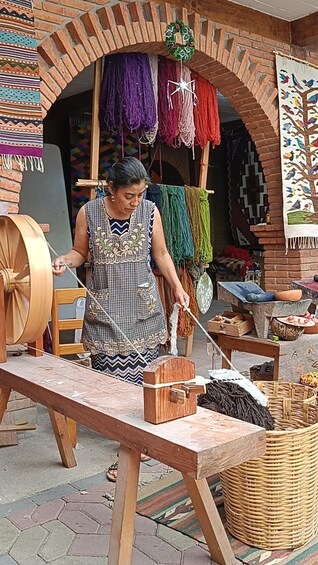 A person weaving with a spindle and distaff, surrounded by colorful yarns and a traditional loom. 5