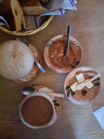 A wooden table with a basket of bread, two ceramic bowls with food, and a spoon. 4