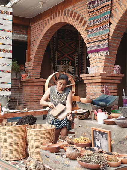 A person seated at a table with various items including baskets, bowls, and a woven chair. 3